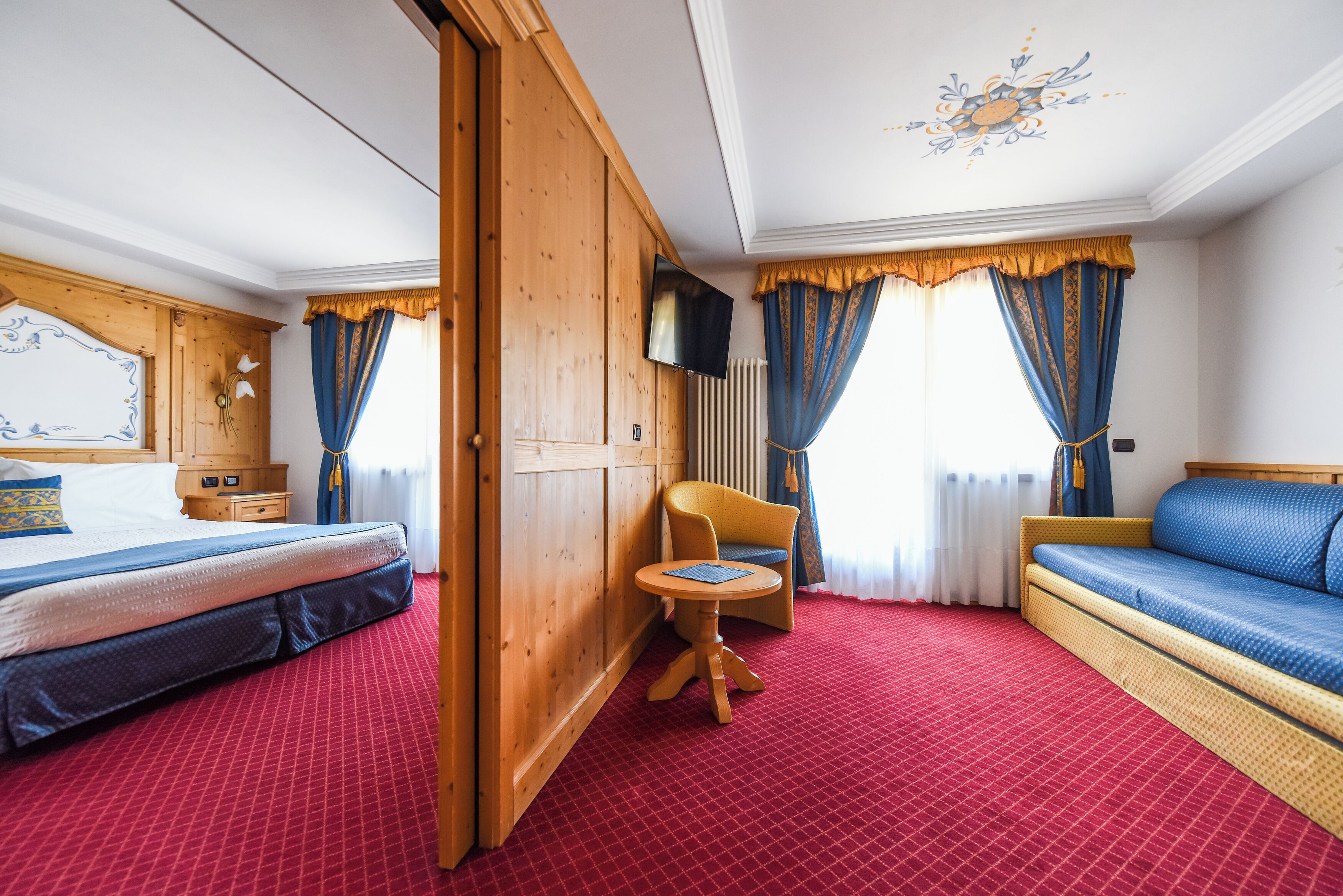 A hotel room with a bed, a sofa, a small table, and a television.