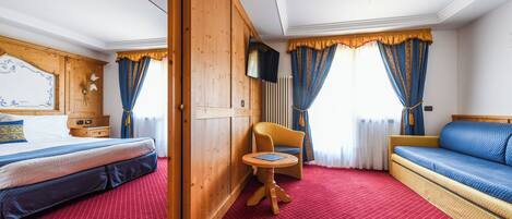 A hotel room with a bed, a sofa, a small table, and a television.