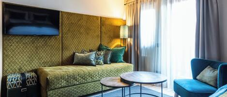 A hotel room with a bed, a TV mounted on the wall, a small table, a chair, and a window with curtains.