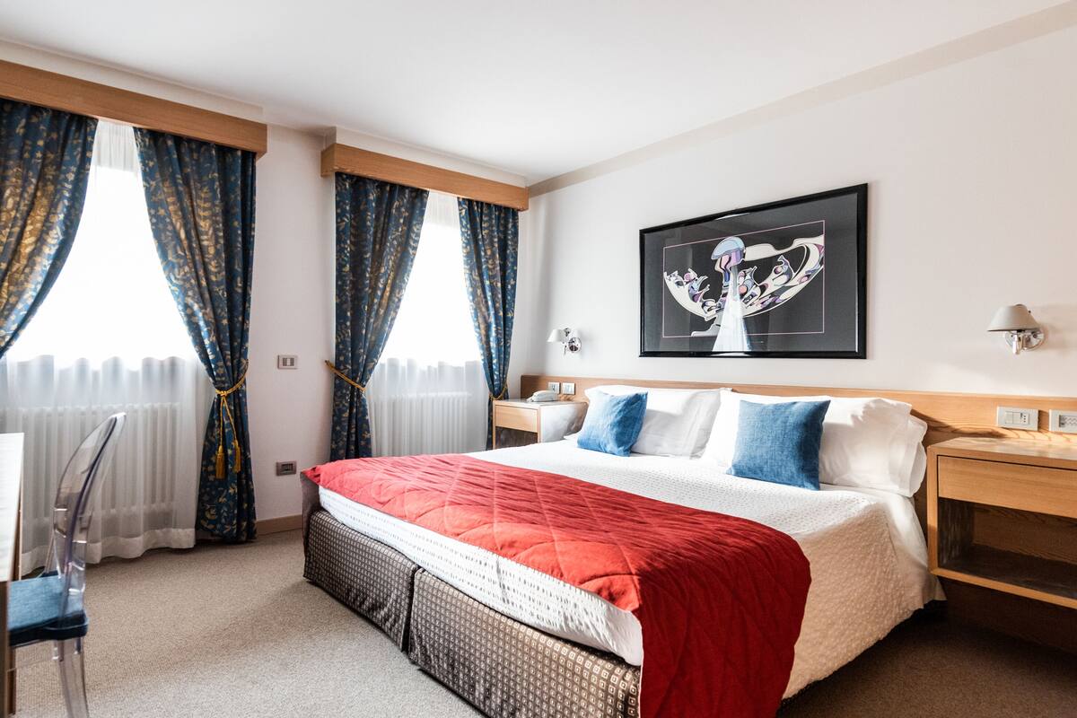 Habitación de hotel con cama, mesita de noche, lámpara y un cuadro en la pared.