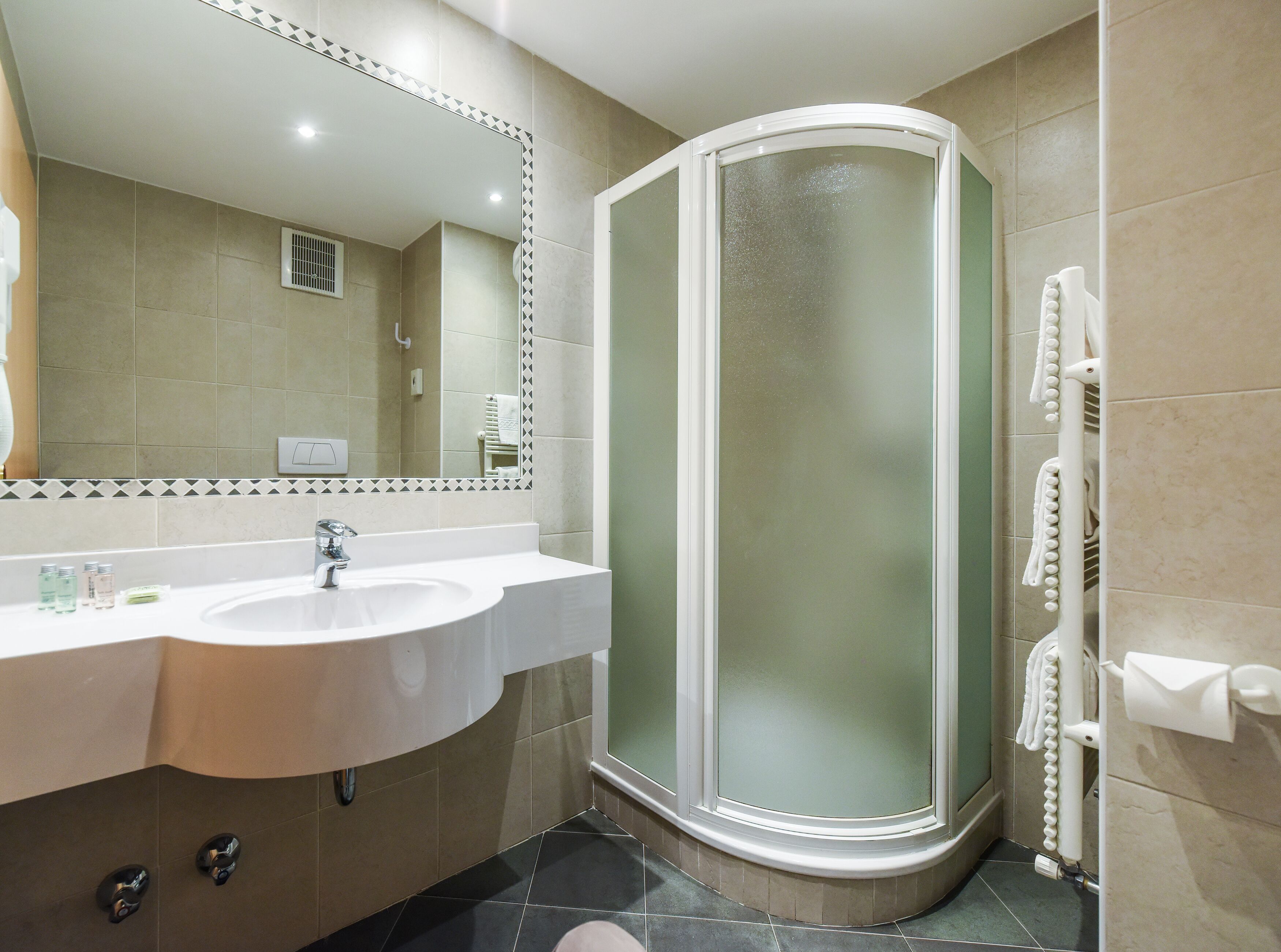 Un baño moderno con cabina de ducha curva, un lavamanos con espejo y un perchero para toallas.