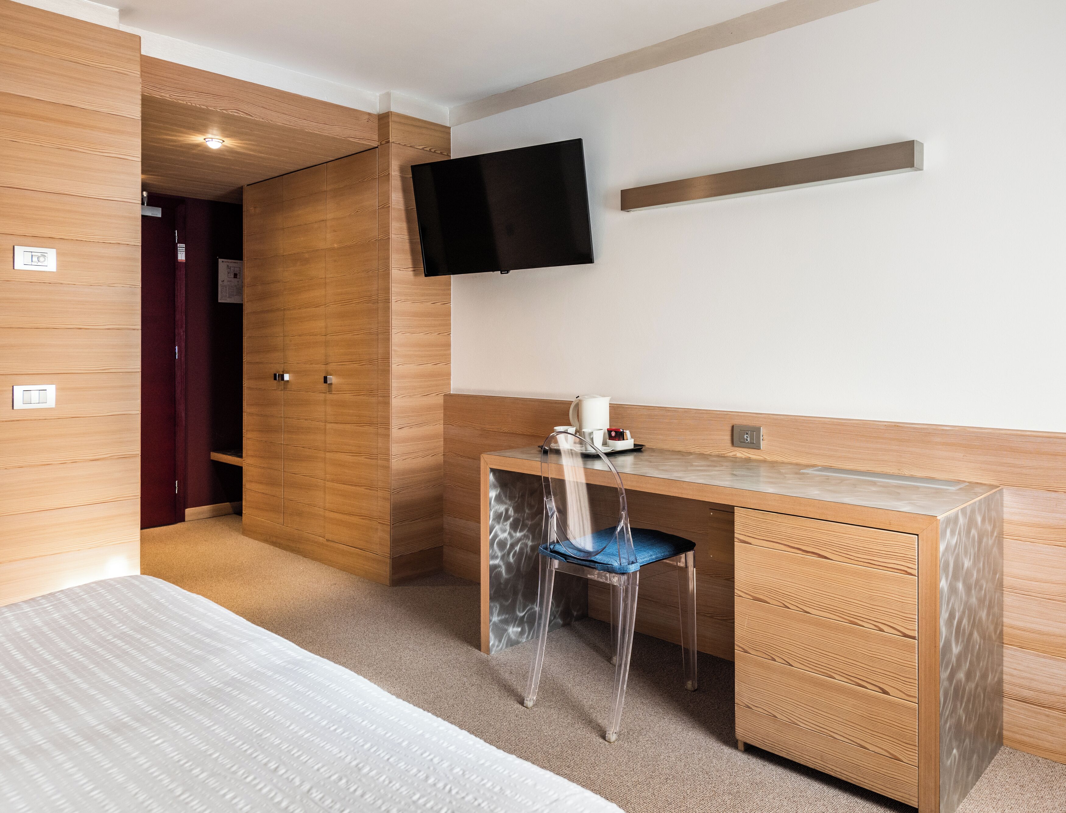 Une chambre d’hôtel équipée d’une armoire en bois, d’un bureau avec une chaise, d’un lit et d’un téléviseur fixé au mur.