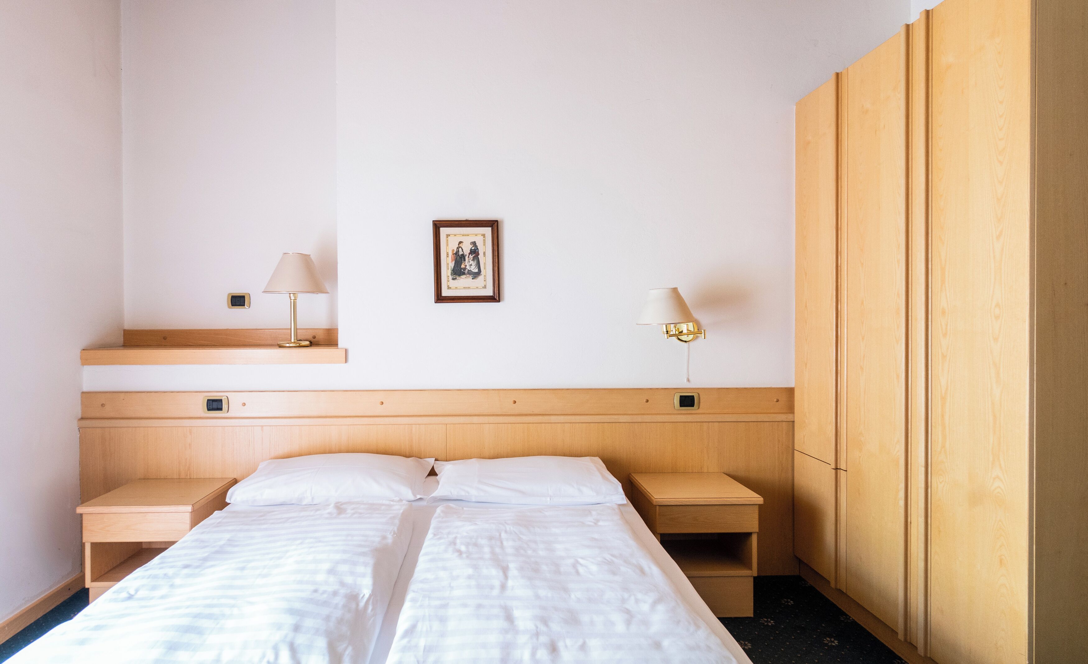 Ein Hotelzimmer mit einem Bett, zwei Nachttischen, einem Holzschrank und zwei Wandleuchten.