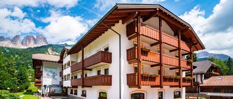 Un hotel de varios pisos con balcones y un paisaje montañoso de fondo.
