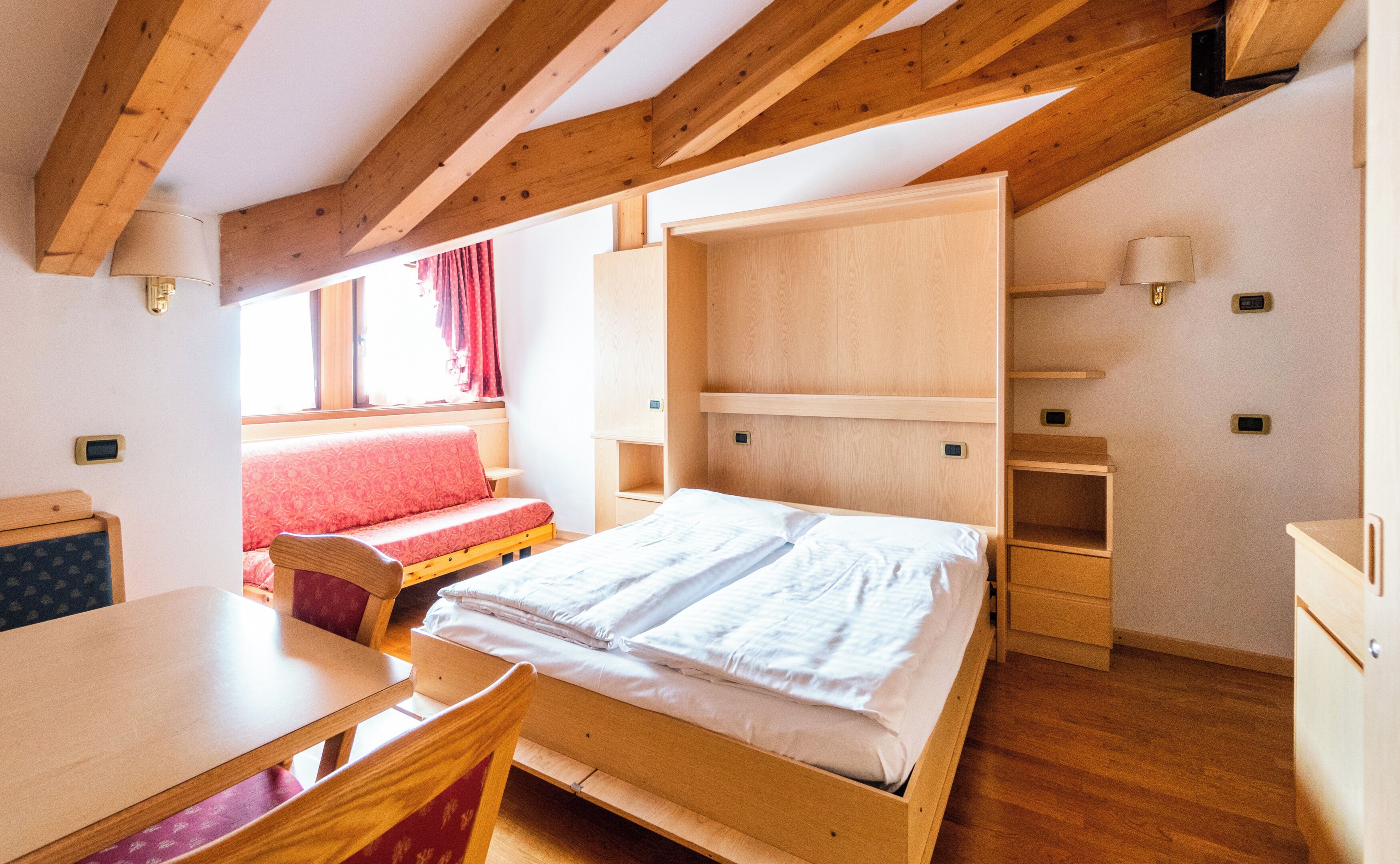 A room with a bed, a desk, a chair, and a window with curtains.