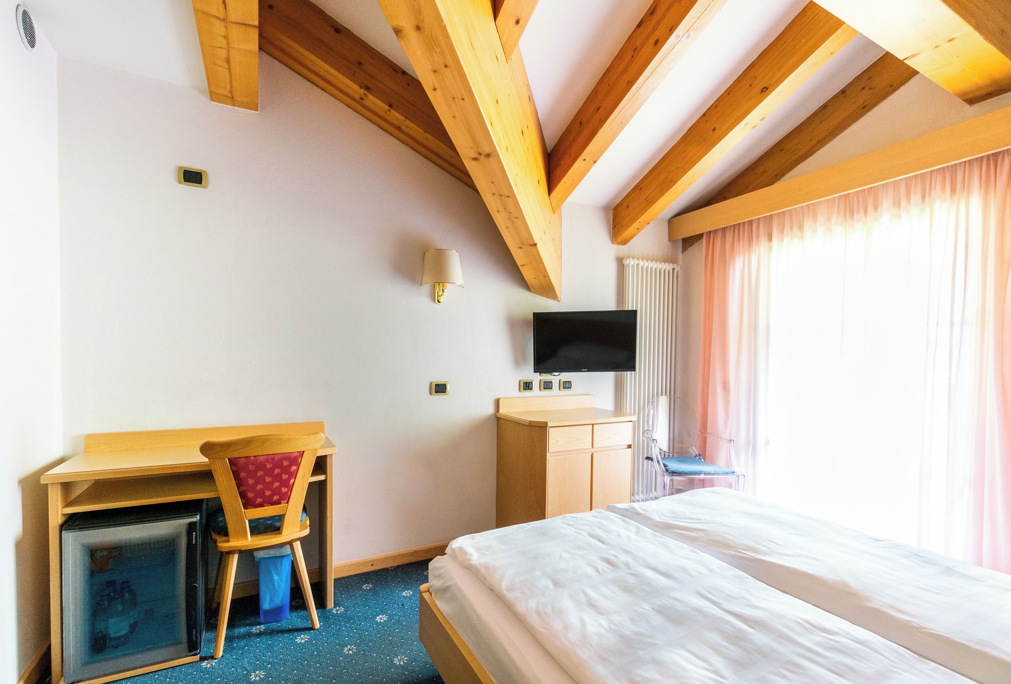 Une chambre d’hôtel comprenant un lit, un bureau avec une chaise, une télévision et un petit réfrigérateur.