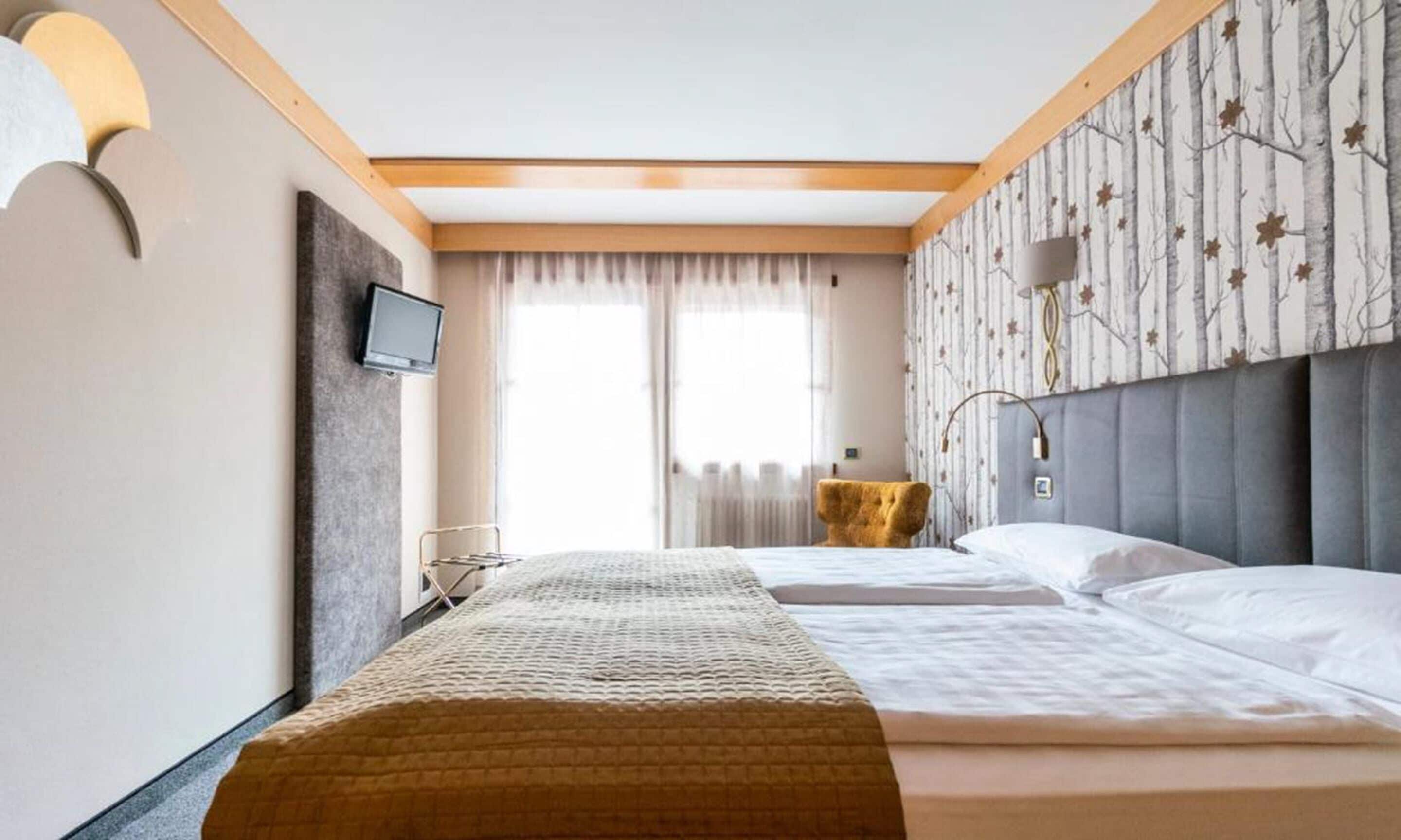 Ein Hotelzimmer mit Bett, Fernseher, kleinem Tisch und einem Fenster mit Vorhängen.