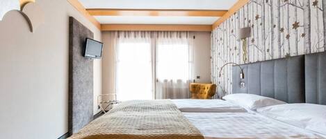 A hotel room with a bed, a TV, a small table, and a window with curtains.