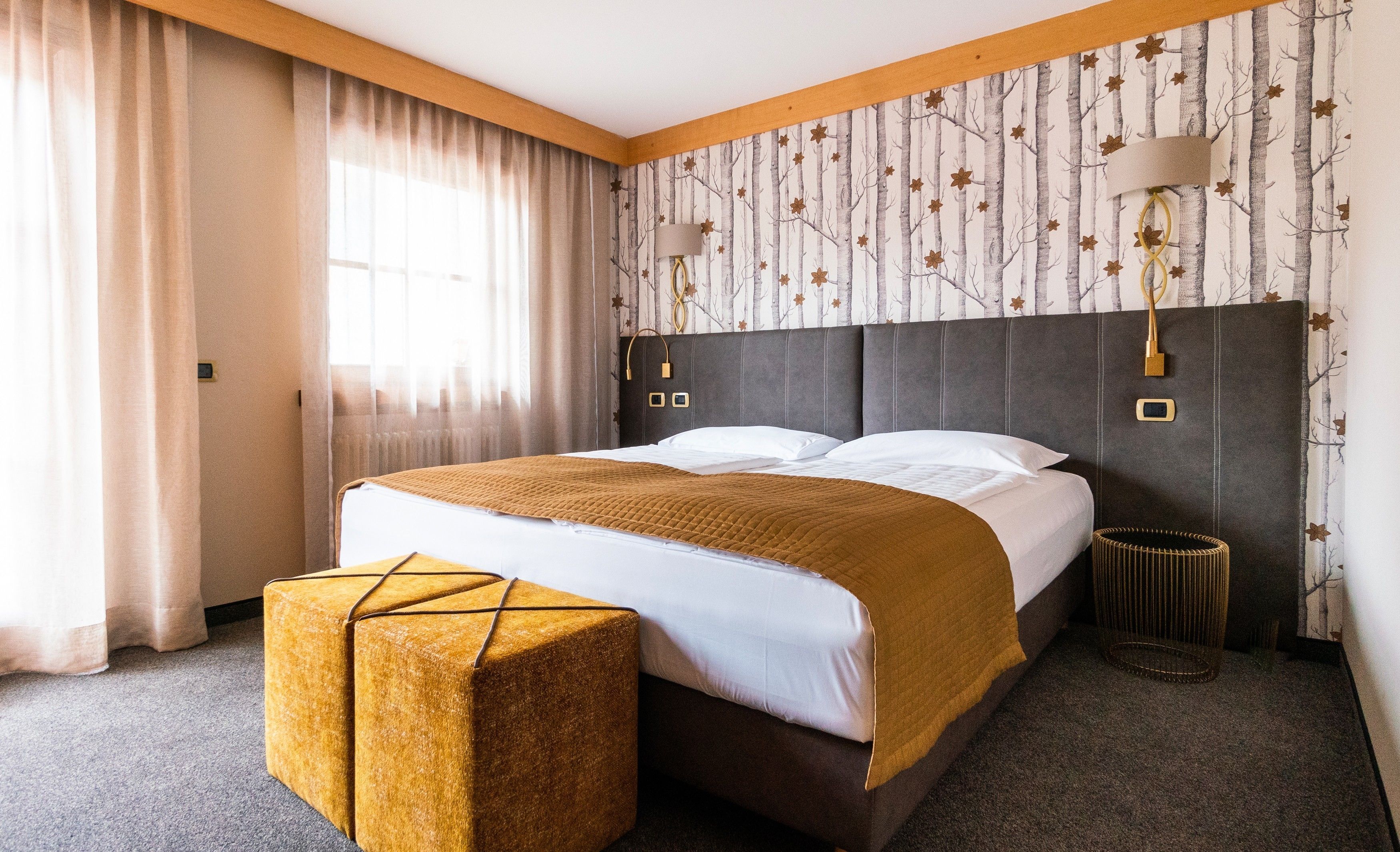 Hotelkamer met een groot bed, nachtkastje, lamp en raam met gordijnen.