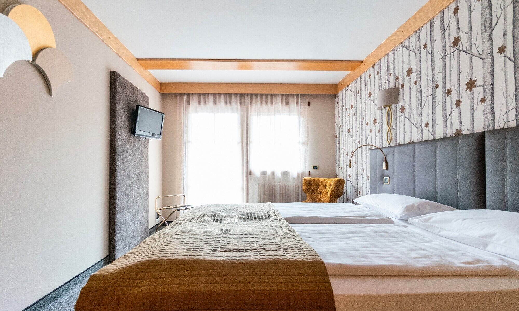Habitación de hotel con una cama grande, un televisor montado en la pared y una ventana con cortinas.