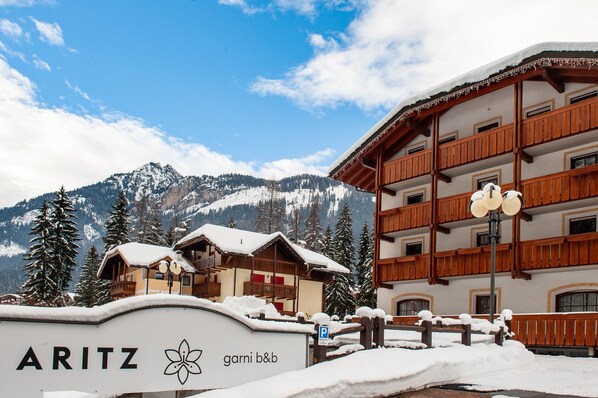 A hotel with a snow-covered exterior, wooden balconies, and a mountain backdrop. - Aritz (Campitello di Fassa)