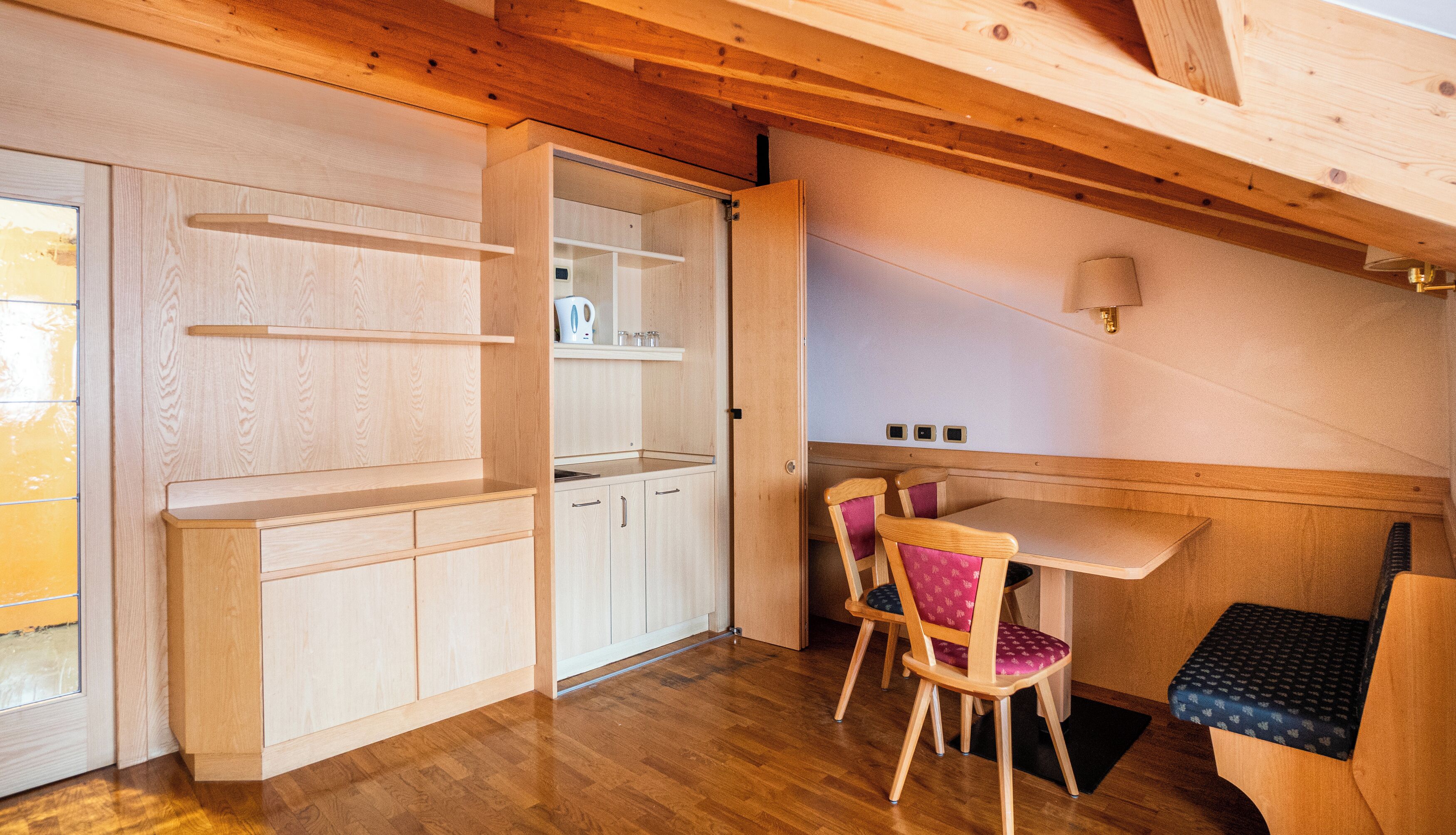 A compact kitchen with wooden cabinets, a dining area with a table and chairs, and a small window.