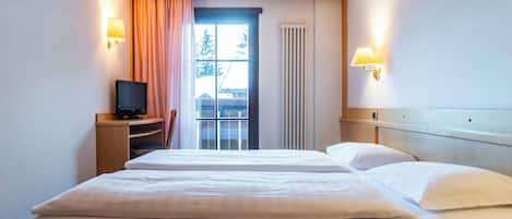 Een hotelkamer met een bed, een televisie op een standaard, een raam met gordijnen en wandlampen.
