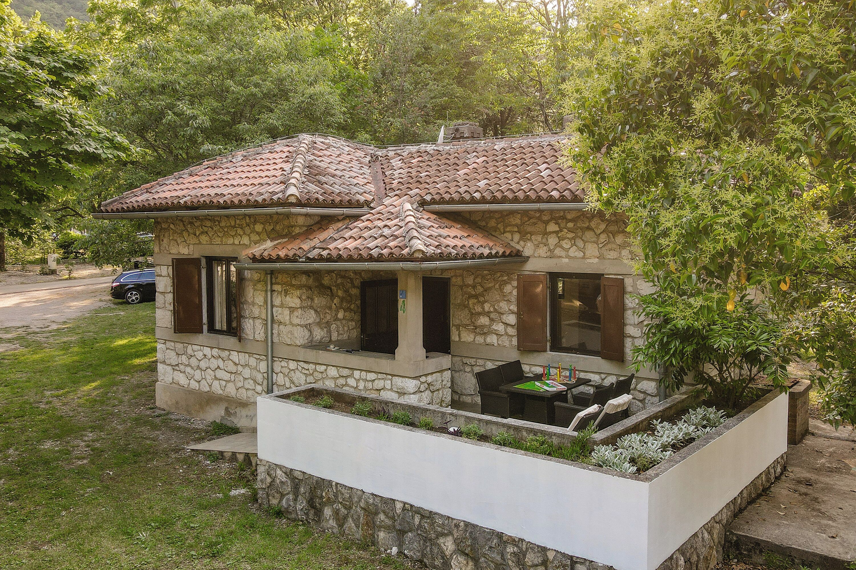 A stone house with a tiled roof, a porch with outdoor seating, and a garden area.