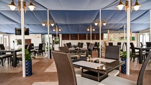 An indoor patio area with wicker furniture, tables, and chairs under a blue canopy. - Holiday Resort Medveja - Liburnia (Lovran)