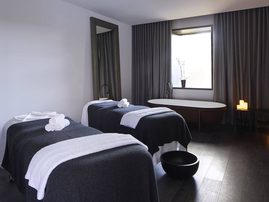 A hotel room with two beds, a bathtub, a small table, and a window with curtains.