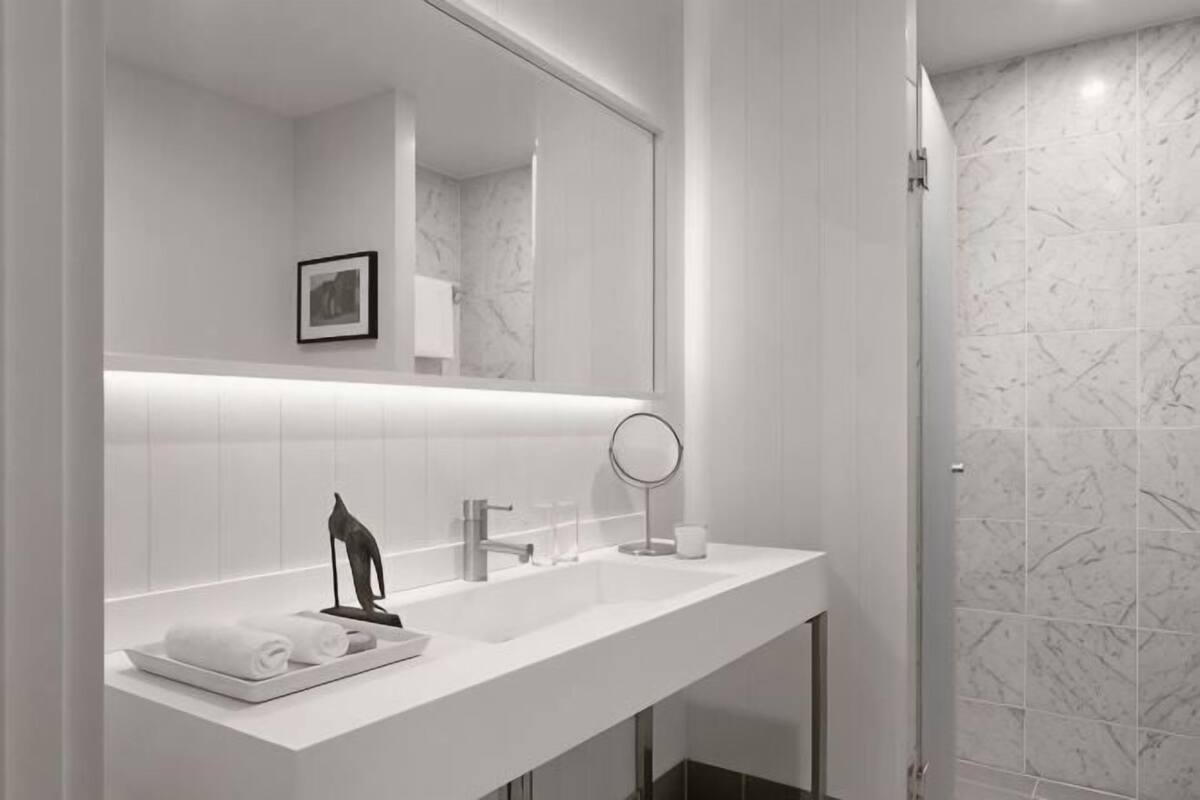 A modern bathroom with a white vanity, a large mirror, and a shower area with marble tiles.