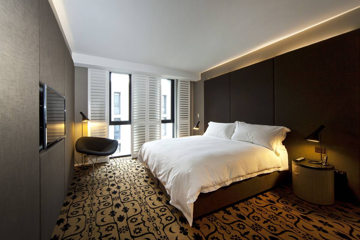 A modern bedroom with a large bed, a chair, and a nightstand.