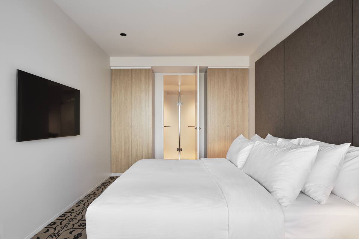A modern bedroom with a large bed, a flat-screen TV mounted on the wall, and a wardrobe with a sliding door.
