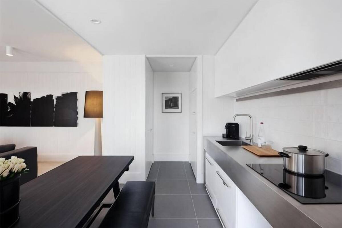 A modern kitchen with a dark countertop, a stove, and a sink. There is a dining area with a bench and a table.
