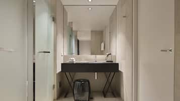 Un baño moderno con un tocador oscuro, un espejo grande y un cubo de basura negro.