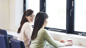Dos personas sentadas a una mesa junto a una ventana en una habitación de diseño sencillo, con vistas al exterior.