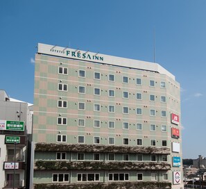 Un hôtel à plusieurs étages, doté d’une façade à motifs géométriques, de nombreuses fenêtres et d’enseignes indiquant différents commerces.