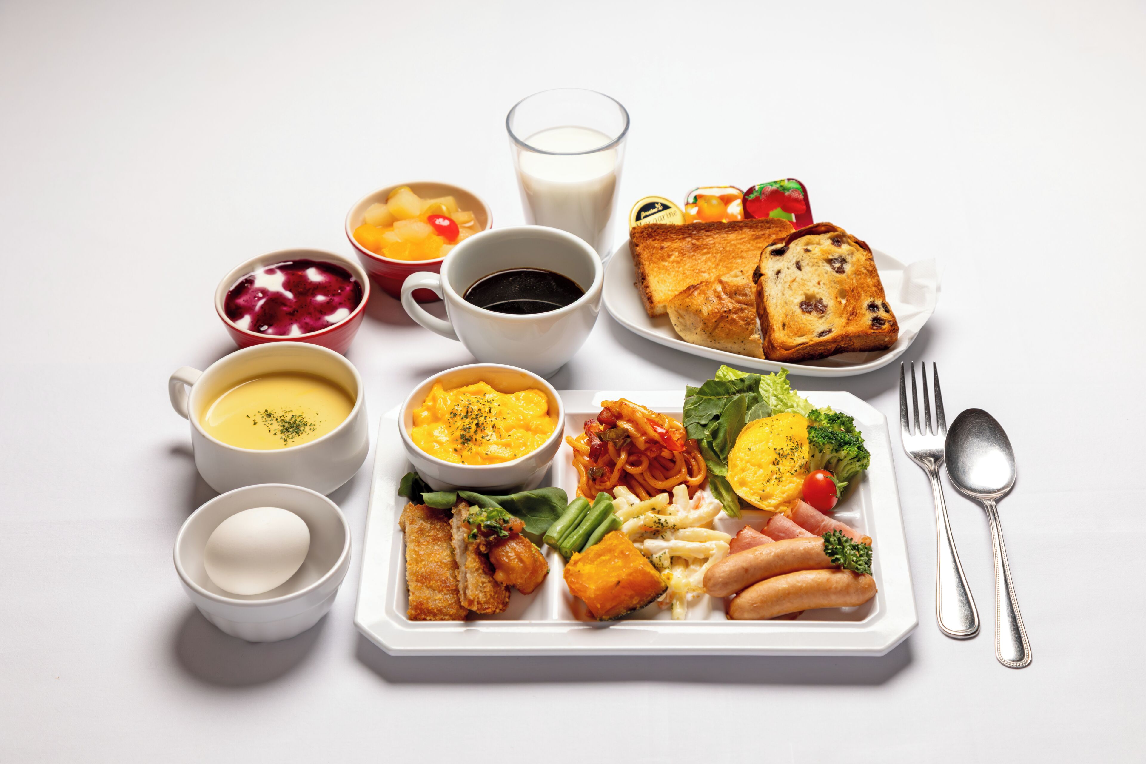 A white plate with a variety of food items including bread, vegetables, and a salad, accompanied by several cups of beverages and a glass of milk.