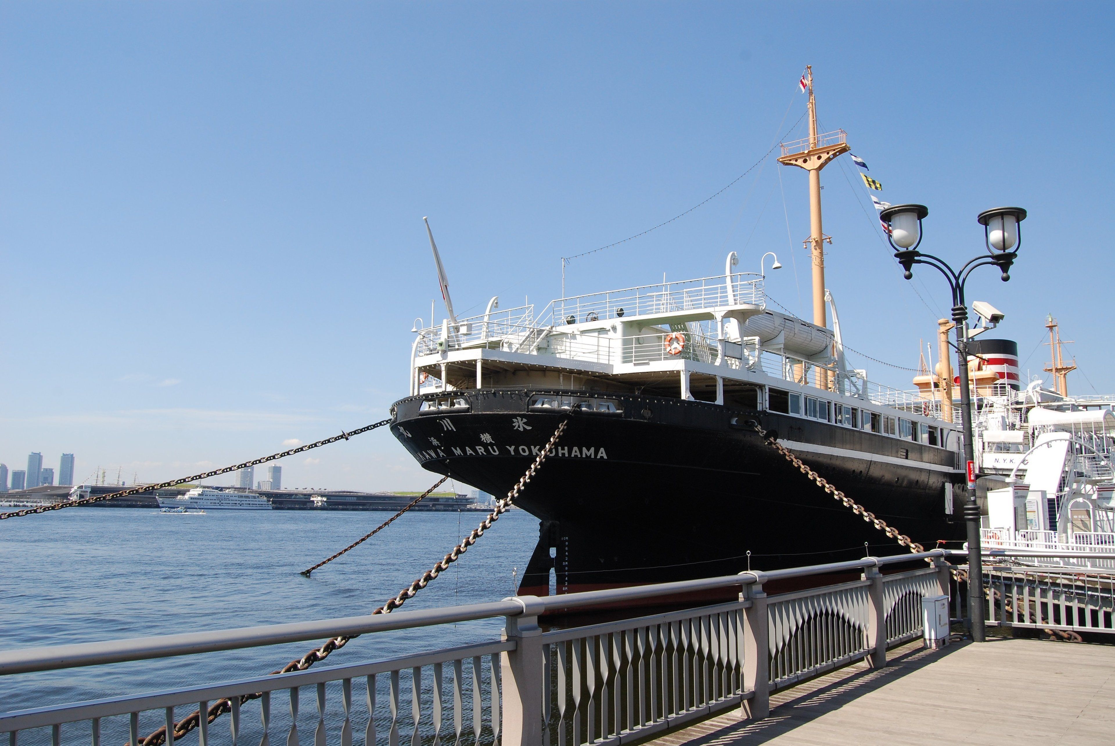 A large ship docked at a pier with a city skyline in the background.