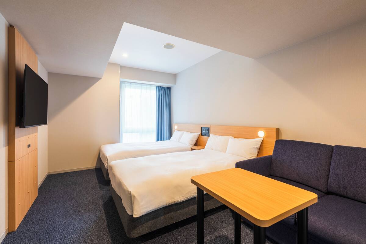 Een hotelkamer met twee bedden, een bank, een televisie en een kleintje tafeltje.