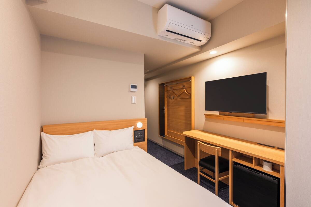 Een hotelkamer met een bed, nachtkastje, televisie, kledingkast en airconditioning.