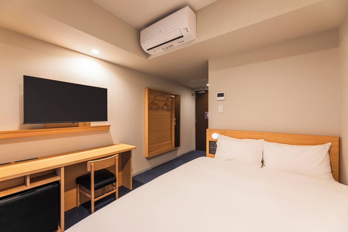 Een hotelkamer met een bed, een bureau met stoel, een televisie en een airconditioning.