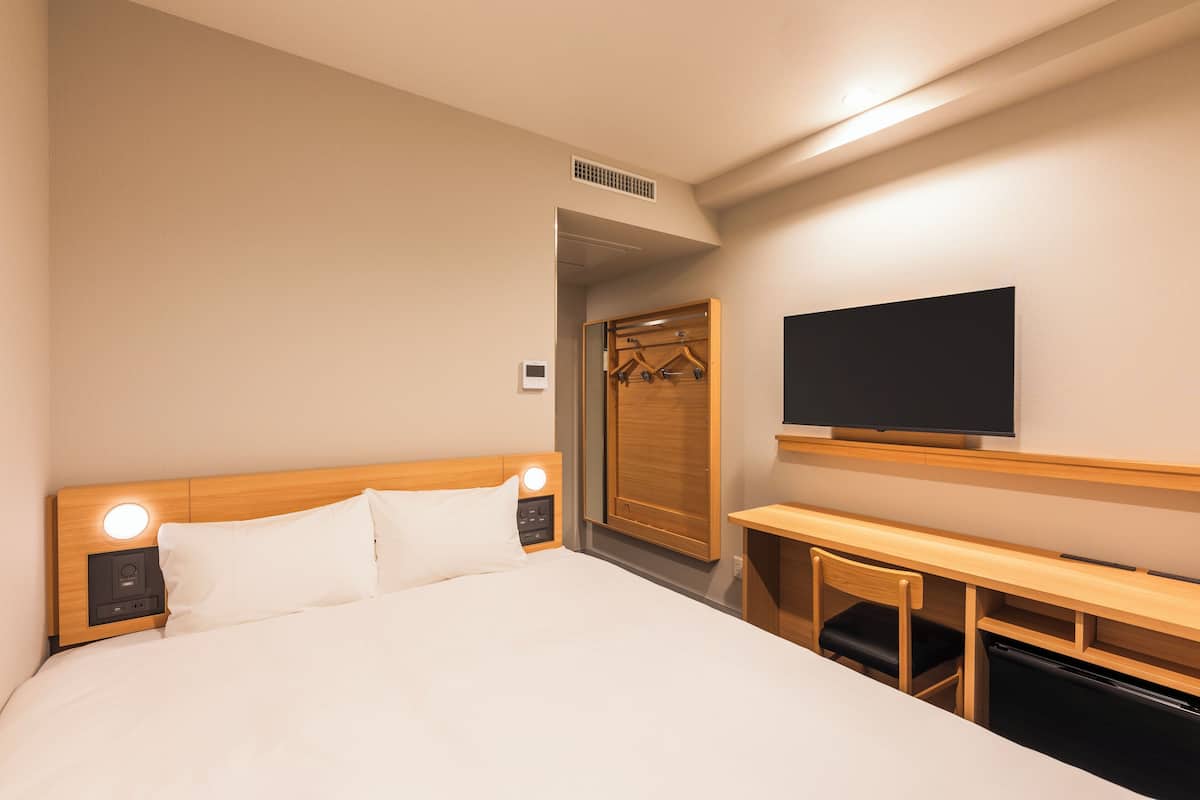 Ein Hotelzimmer mit Bett, Nachttisch, Fernseher und Schreibtisch mit Stuhl.