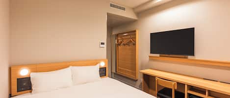 A hotel room with a bed, bedside table, TV, and a desk with a chair.