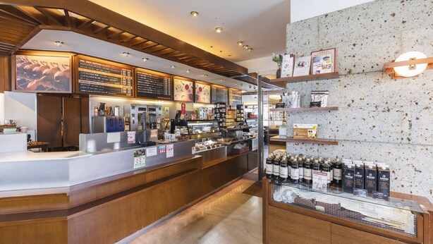 L’intérieur d’un café, avec un comptoir, des panneaux affichant le menu et des étagères remplies de boissons.