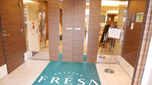 L’entrée d’un hôtel, avec un tapis vert sur lequel on peut lire les mots « FRESA INN » et « Fresh-Sense Amenity ».