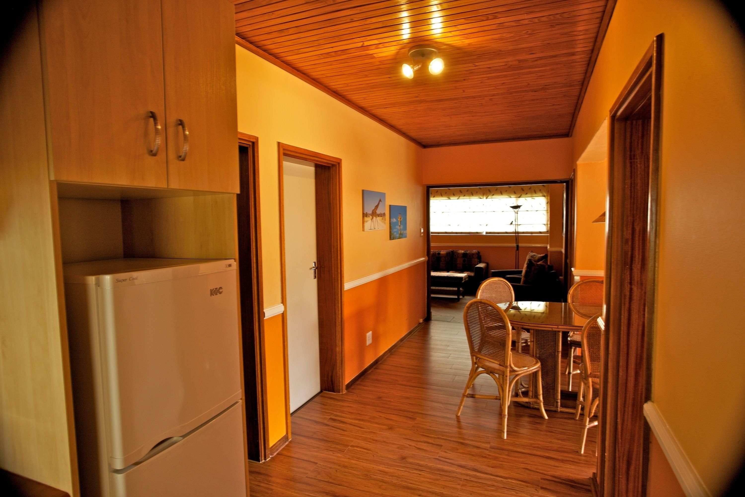Una cocina con gabinetes de madera y un refrigerador, un comedor con mesa y sillas, y una ventana con persianas.