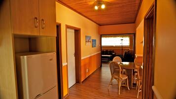 Una cocina con gabinetes de madera y un refrigerador, un comedor con mesa y sillas, y una ventana con persianas.