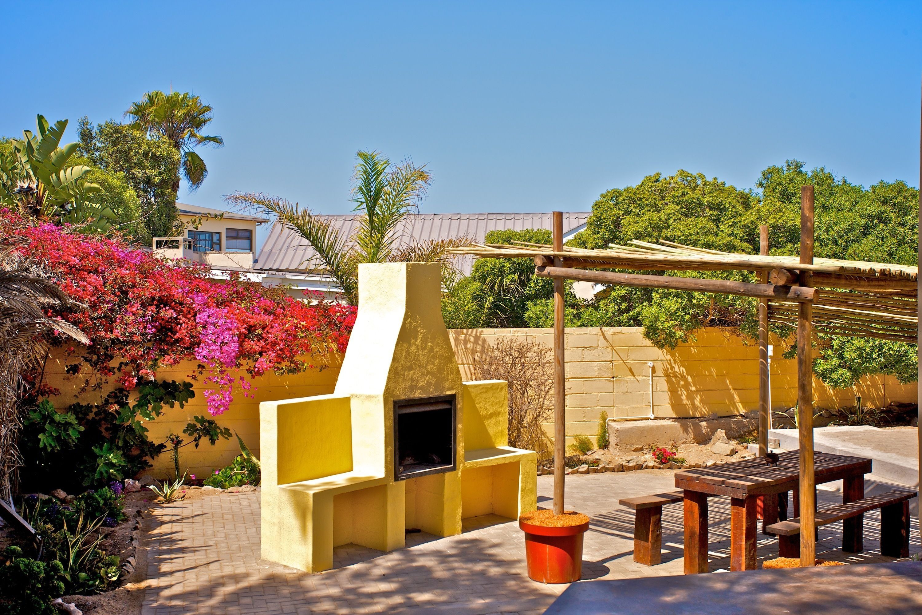 Un patio exterior con una parrilla, bancos de madera y plantas en macetas.