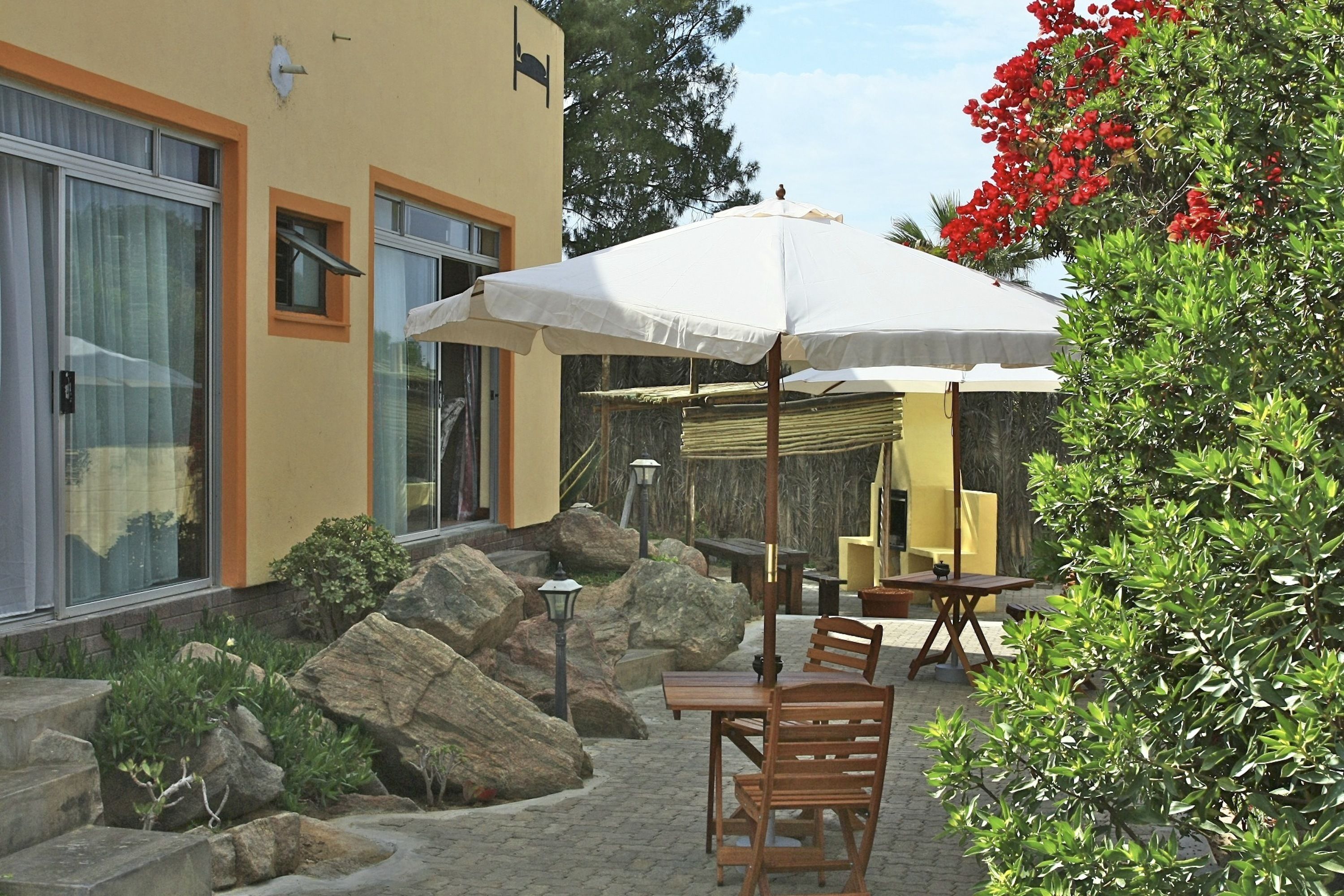 Un patio al aire libre con una mesa, sillas, un paraguas blanco y un jardín de rocas.