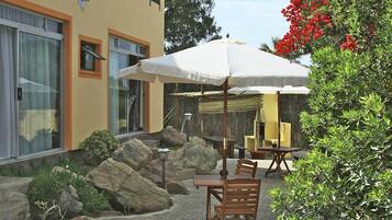 An outdoor patio with a table and chairs, a white umbrella, and a rock garden.