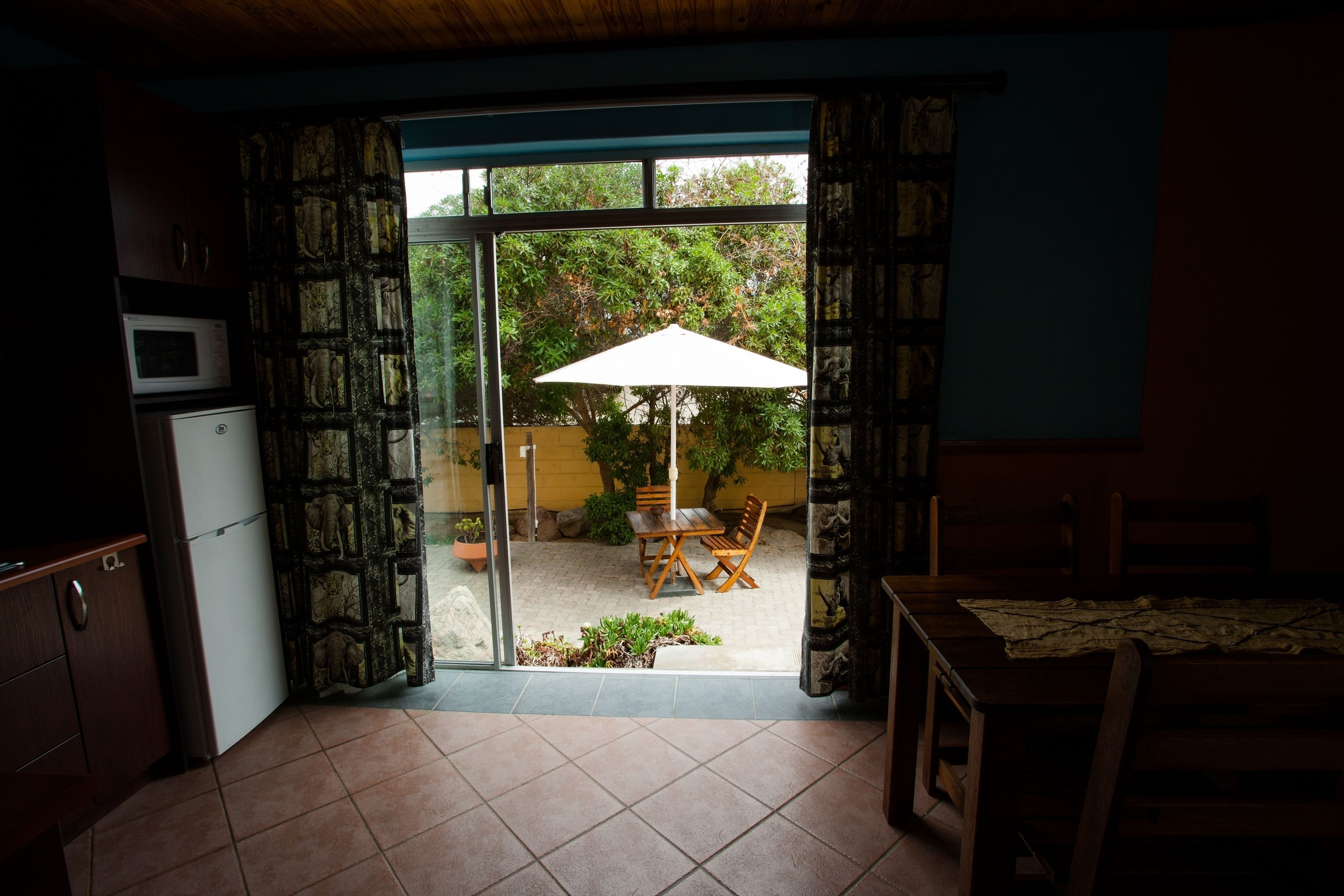Una cocina con una puerta de vidrio corrediza que da a un patio exterior con mesa y sillas, y un refrigerador pequeño.