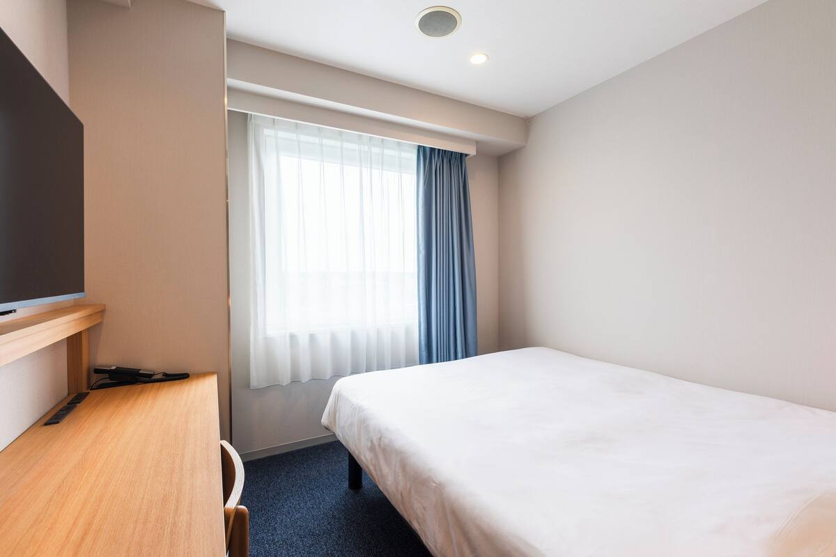 A hotel room with a bed, a desk, and a window with curtains.