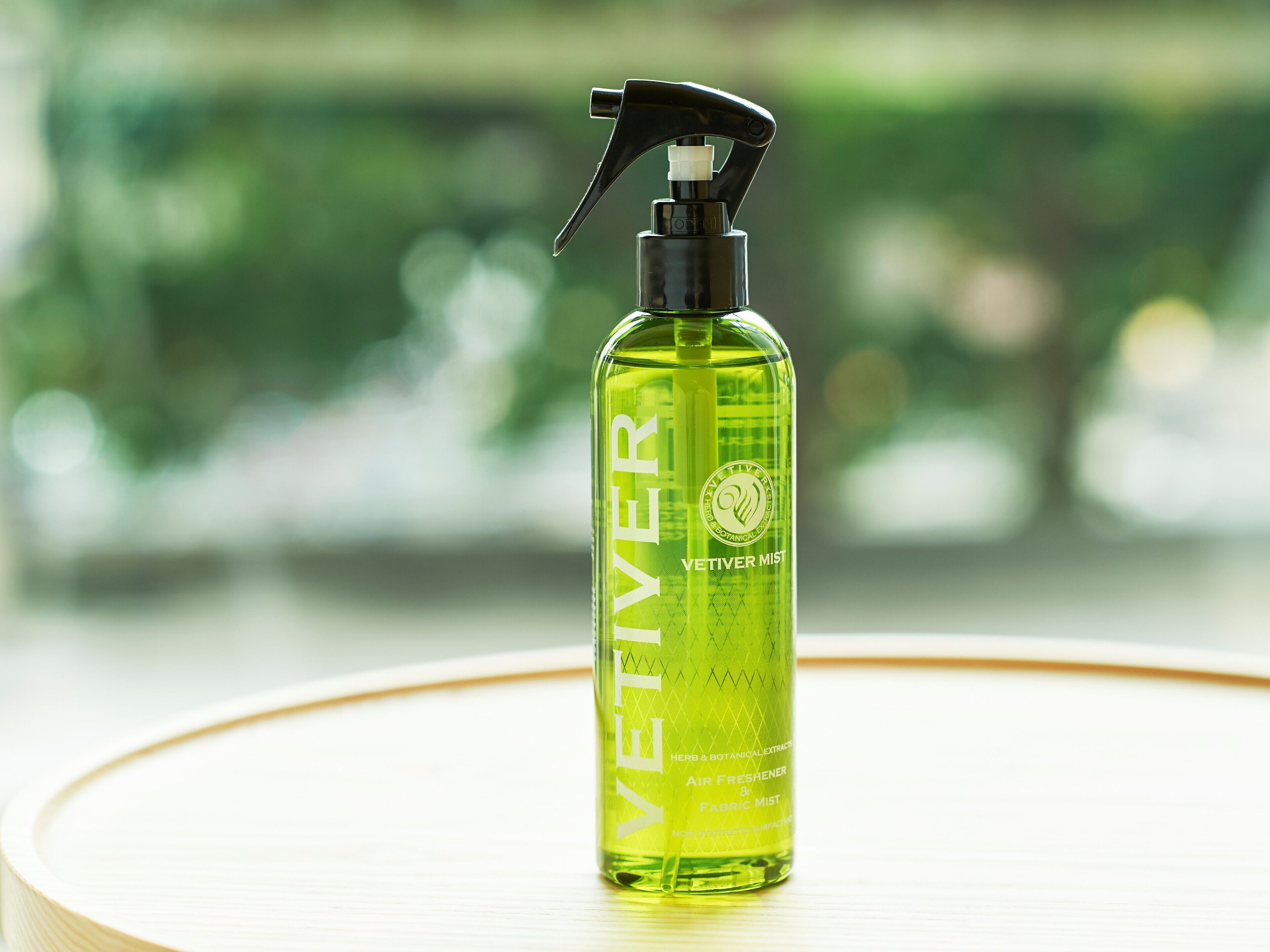 Een fles VETIVER mist op een rond tafel tegen een vage groene achtergrond.