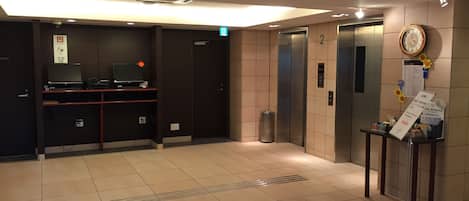 A modern elevator area with a digital clock, a trash bin, and a small table with informational signs.