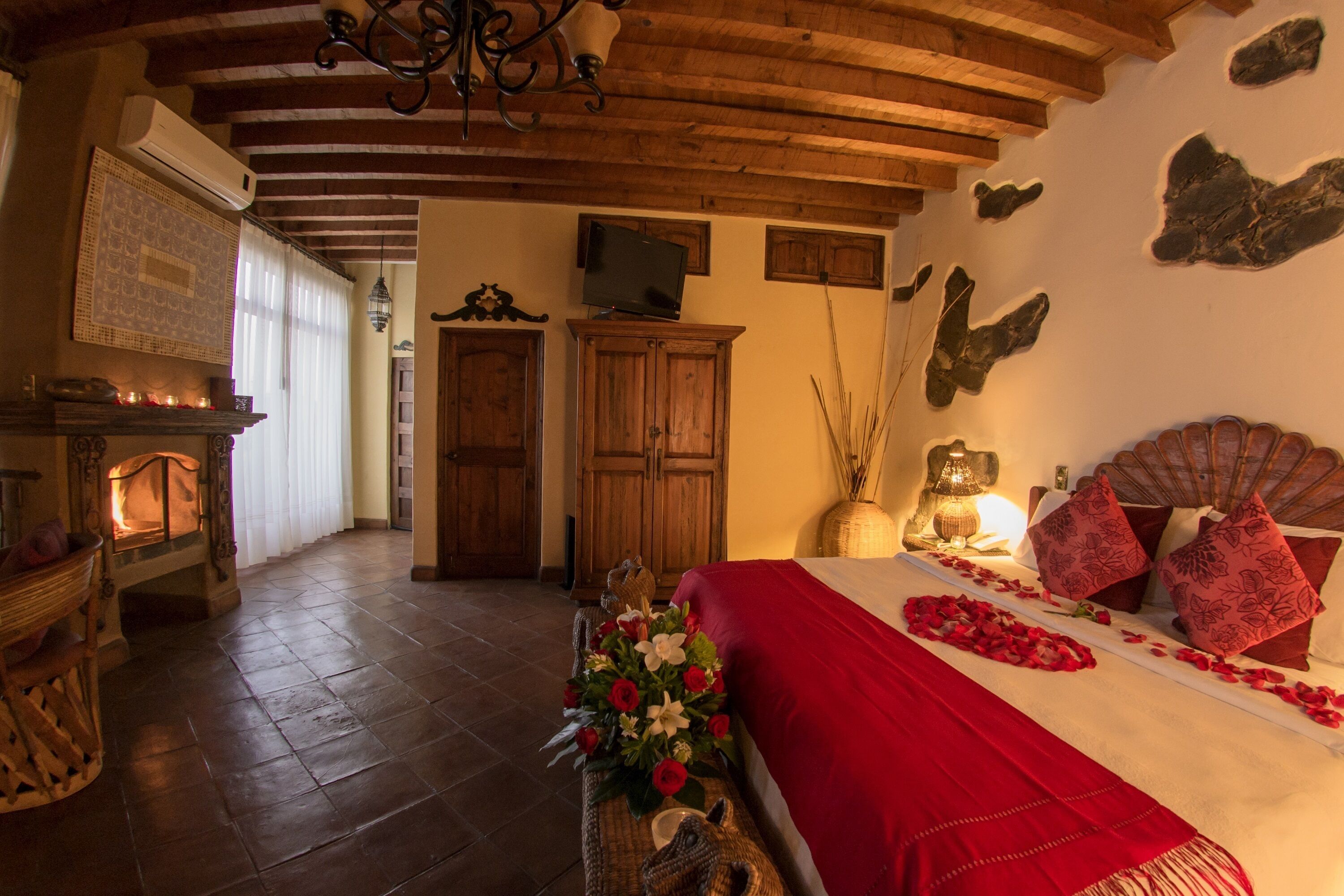 A cozy room with a fireplace, wooden furniture, a bed with red bedding, and a decorative wall.