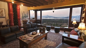 A cozy living room with leather sofas, a wooden coffee table, and a large window offering a scenic view of a lake and mountains. - Hotel Porton Del Cielo (Patzcuaro)