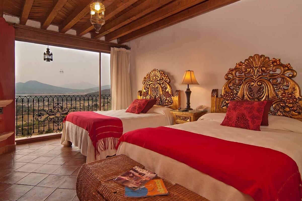 A hotel room with two beds, a balcony with a view, and a wooden ceiling.