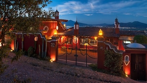 A traditional building with a red facade, a gated entrance, and a view of mountains in the background. - Hotel Porton Del Cielo (Patzcuaro)
