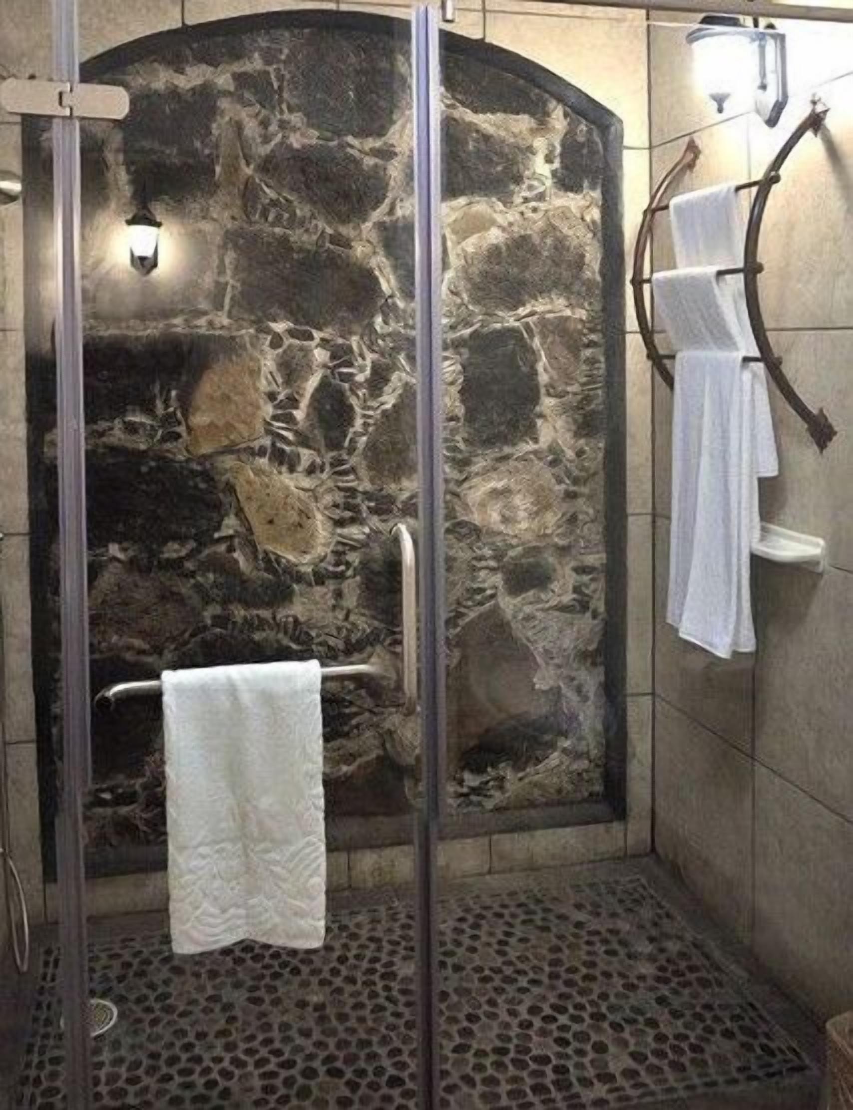 A shower with a stone wall, a glass door, and a towel rack.